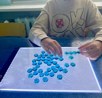 uczeń układa na szkle niebieskie pionki